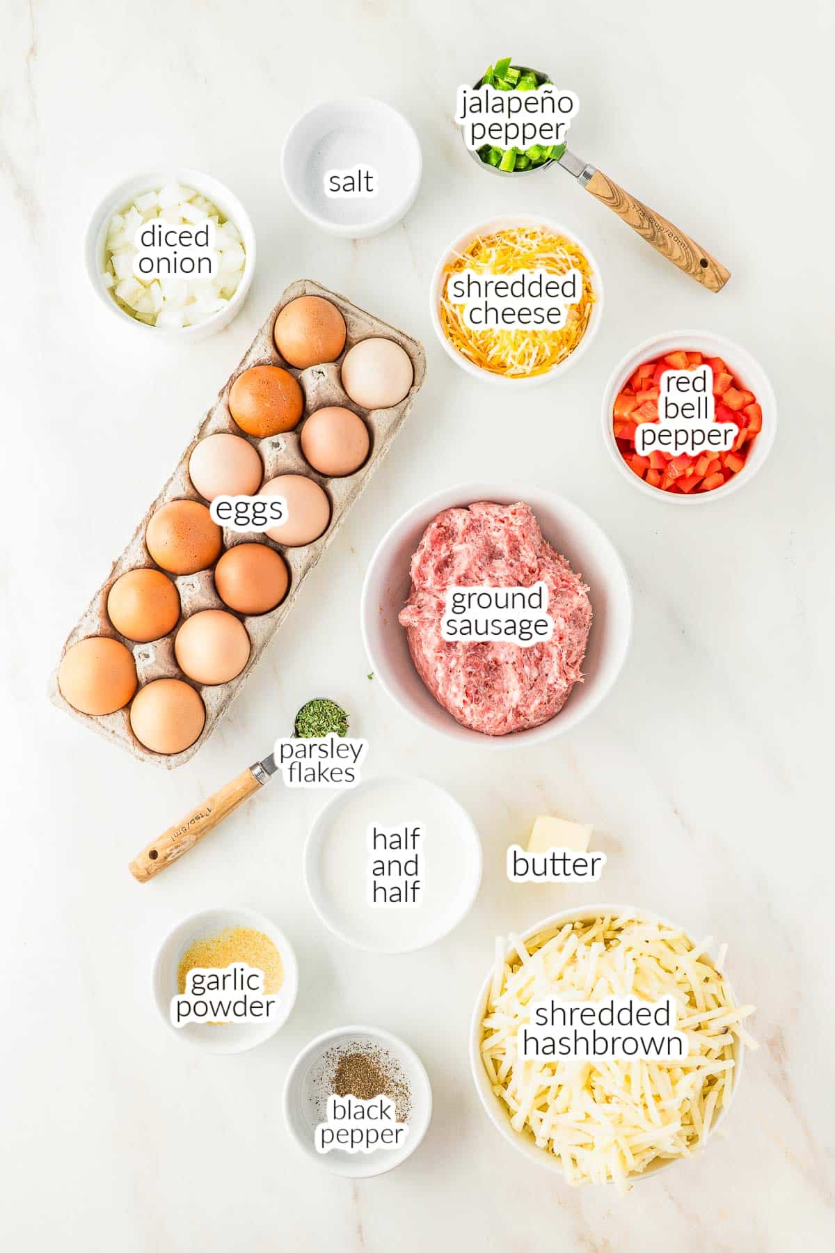 Ingredients for slow cooker breakfast casserole arranged on a counter, including eggs, ground sausage, shredded hashbrowns, cheese, bell pepper, onion, jalapeño, parsley, butter, half and half, and spices.