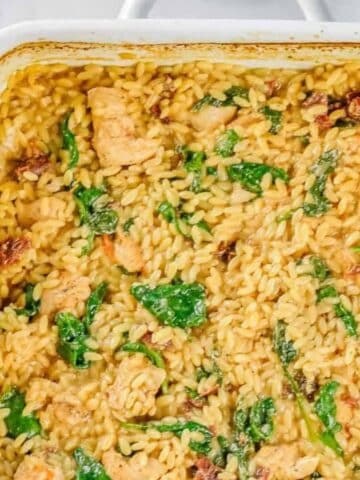 Baked casserole dish filled with cooked orzo pasta, pieces of chicken, spinach, and sun-dried tomatoes in a creamy sauce.
